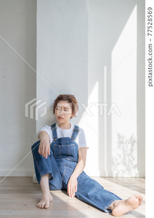 Genderless LGBT boy-like girl wearing overalls and sitting on the floor 77528569