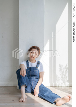 Genderless LGBT boy-like girl wearing overalls and sitting on the floor 77528570