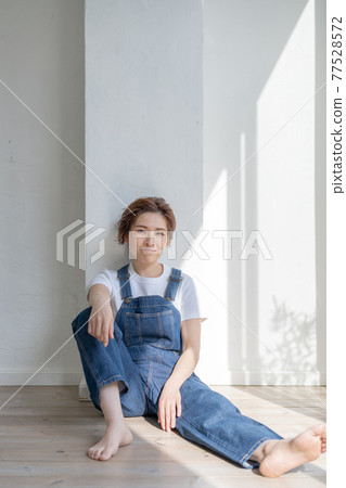 Genderless LGBT boy-like girl wearing overalls and sitting on the floor Genderless LGBT boy-like girl wearing overalls and sitting on the floor 77528572