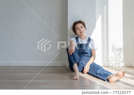 Genderless LGBT boy-like girl wearing overalls and sitting on the floor 77528577