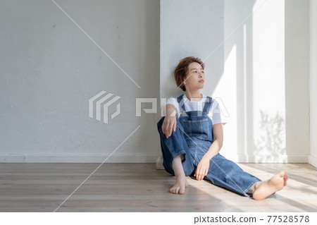 Genderless LGBT boy-like girl wearing overalls and sitting on the floor 77528578