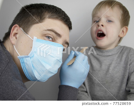 An otolaryngologist examines a child's throat with a wooden spatula. A possible diagnosis is inflammation of the pharynx, tonsils or pharyngitis. The concept of treatment and prevention of childhood An otolaryngologist examines a child's throat with a wooden spatula. A possible diagnosis is inflammation of the pharynx, tonsils or pharyngitis. The concept of treatment and prevention of childhood 77528659