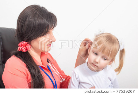 Doctor pediatric otolaryngologist examines the ear of a child of a little girl whose sulfur plug in the ear, background 77529207