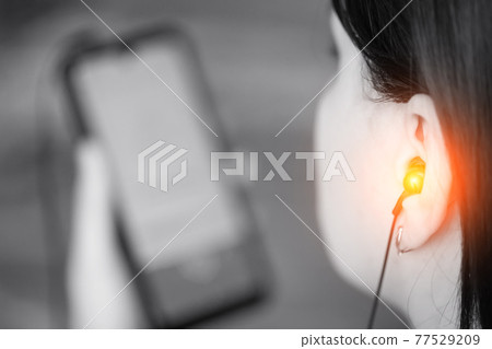 Girl listens to music loudly in headphones from a smartphone, black and white. The concept of the harm of headphones to human hearing at high volume Girl listens to music loudly in headphones from a smartphone, black and white. The concept of the harm of headphones to human hearing at high volume 77529209