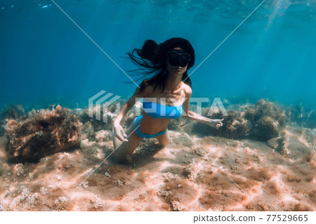 Woman with diving mask posing underwater in transparent ocean with sun rays Woman with diving mask posing underwater in transparent ocean with sun rays 77529665