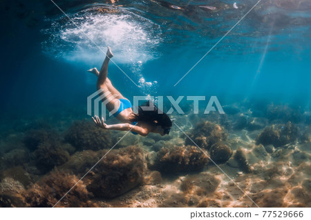 Woman with diving mask posing underwater in transparent ocean with sun rays Woman with diving mask posing underwater in transparent ocean with sun rays 77529666