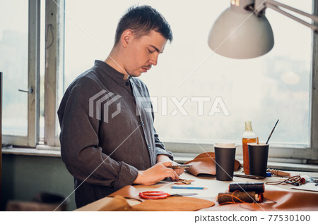 A young apprentice helps his father, glues small leather parts for shoes with a brush in the family workshop A young apprentice helps his father, glues small leather parts for shoes with a brush in the family workshop 77530100