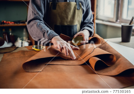 Experienced specialist in the production of footwear leather lays on a table in his workshop 77530165