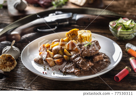 Wild game goulash stew served with roasted potatoes and seasoned with four colour pepper corn. Whole food is surrounded by hunting shotgun and gun bullets Wild game goulash stew served with roasted potatoes and seasoned with four colour pepper corn. Whole food is surrounded by hunting shotgun and gun bullets 77530311