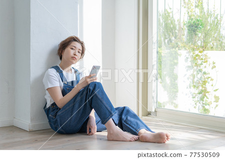 坐在地板上,拿著智能手機的無性別 LGBT 男孩女孩 坐在地板上,拿著智能手機的無性別 LGBT 男孩女孩 77530509