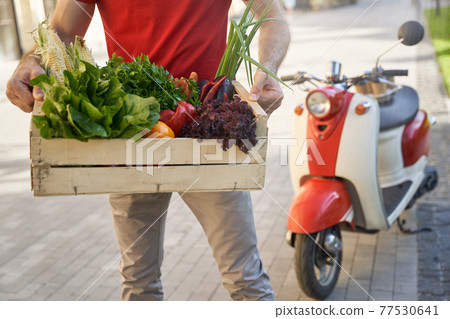 Cropped shot of a male courier in uniform holding grocery box wi 77530641