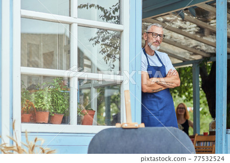 Middle aged caucasian man leaning on garden house wall 77532524