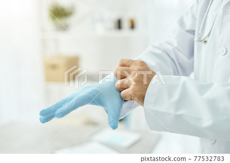 Male doctor putting on blue sterile gloves in clinic 77532783