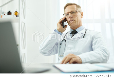Handsome male doctor having phone conversation in clinic 77532817