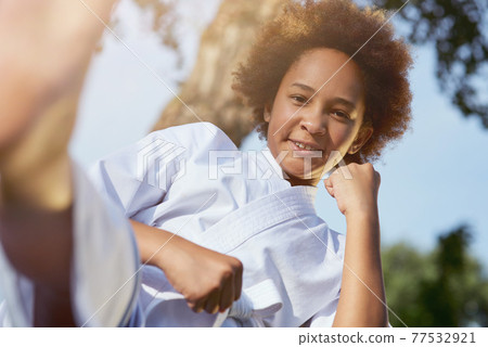 Cheerful Afro American girl practicing martial arts outdoors 77532921