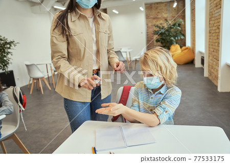 Cropped shot of young female teacher using an alcohol spray to disinfect student hands in classroom Cropped shot of young female teacher using an alcohol spray to disinfect student hands in classroom 77533175