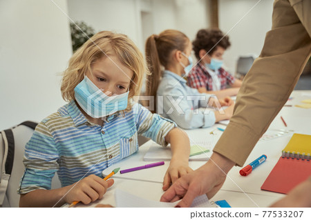 Little boy wearing protective face mask reading the task. Elementary school kids sitting together at the table in a classroom 77533207