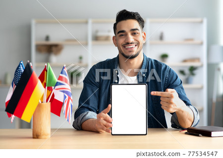Cheerful arab guy pointing at digital tablet with empty screen Cheerful arab guy pointing at digital tablet with empty screen 77534547