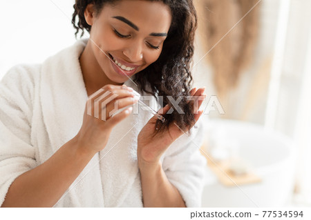 African American Woman Applying Serum On Damaged Hair In Bathroom 77534594