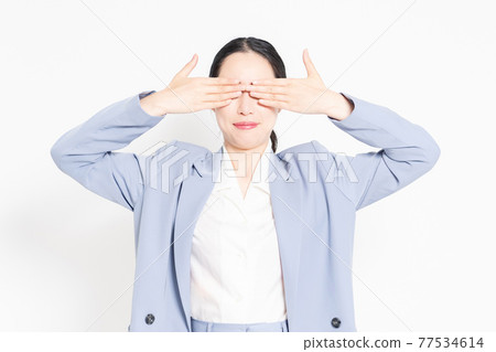 A woman standing in front of a white background and hiding her eyes 77534614