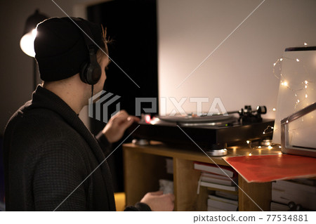 Young unshaven handsome hipster guy push start button on turntable backlit Young unshaven handsome hipster guy push start button on turntable backlit 77534881