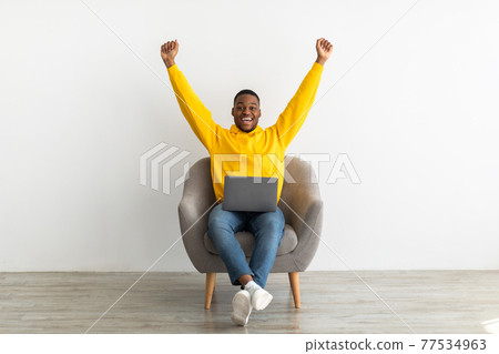 Joyful African Guy With Laptop Shaking Fists Over Gray Wall 77534963