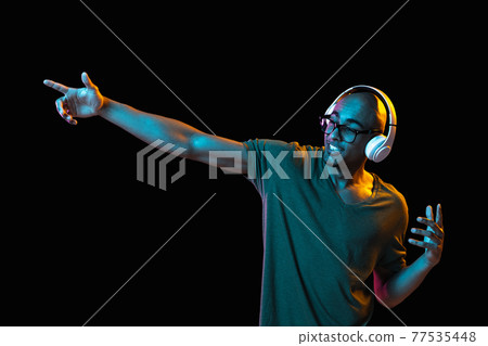 African-american young man's portrait on dark studio background in neon. Concept of human emotions, facial expression, youth, sales, ad. 77535448