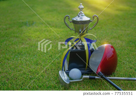 Golf champion trophy on green grass with golf clubs and golf ball in beautiful golf course. 77535551