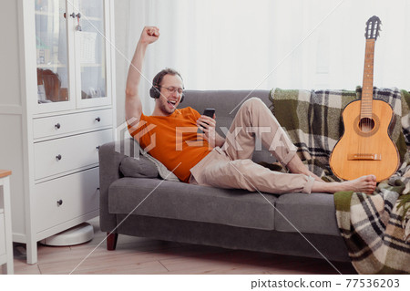 Handsome man playing on the guitar on the couch at home Handsome man playing on the guitar on the couch at home 77536203