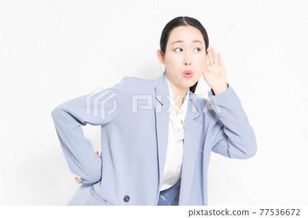 A woman standing in front of a white background and listening A woman standing in front of a white background and listening 77536672