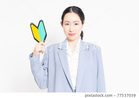 一個站在白色背景前,拿著初學者標記的女人 一個站在白色背景前,拿著初學者標記的女人 77537039