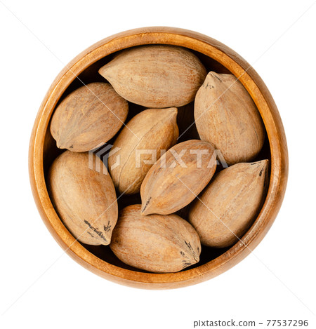 Unshelled pecan nuts, in a wooden bowl. Whole pecans, seeds and edible nuts of Carya illinoinensis. Used as a snack and in various recipes. Close-up, from above, isolated over white, macro food photo. Unshelled pecan nuts, in a wooden bowl. Whole pecans, seeds and edible nuts of Carya illinoinensis. Used as a snack and in various recipes. Close-up, from above, isolated over white, macro food photo. 77537296