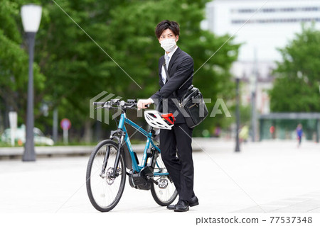 A young man in a mask who stops his bicycle A young man in a mask who stops his bicycle 77537348