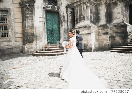 A loving wedding couple are walking back along the streets of the city of Lviv 77538037