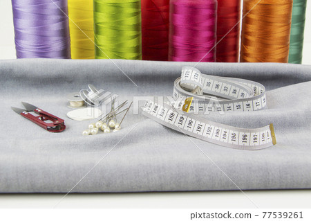 Colorful sewing threads, tailor's scissors and measuring tape in the foreground. 77539261