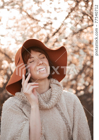 Young smiling girl in a hat on a background of flowering trees 77540712