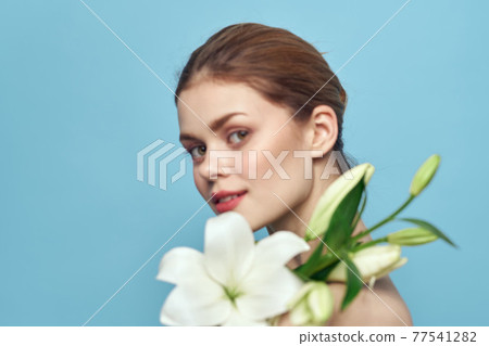 Woman with white flower on blue background cropped view of naked shoulders Woman with white flower on blue background cropped view of naked shoulders 77541282