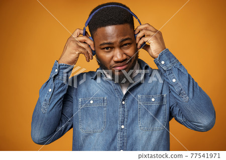 Handsome young african american man listening to music with blue headphones Handsome young african american man listening to music with blue headphones 77541971