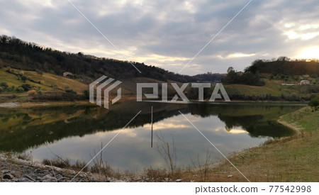 Reflections in a small lake immersed in the green hills of the Marche 77542998
