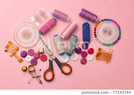 Sewing accessories including thread spools and pins on pink background 77543744