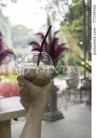 Iced coffee in her hand with garden background Iced coffee in her hand with garden background 77548502