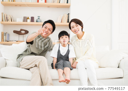 一家三口父母和孩子坐在沙發上指著電視屏幕 一家三口父母和孩子坐在沙發上指著電視屏幕 77549117