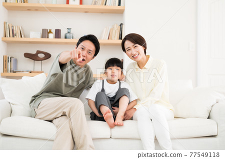 一家三口父母和孩子坐在沙發上指著電視屏幕 77549118