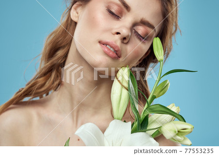 Woman with a bouquet of white flowers on a blue background naked shoulders beautiful face 77553235