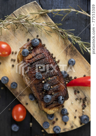 Goose breast Christmas roast with blueberries, tomatoes, red peppers and rosemary served on a wooden board 77553389
