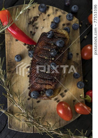 Goose breast Christmas roast with blueberries, tomatoes, red peppers and rosemary served on a wooden board 77553396