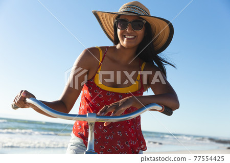 Happy mixed race woman having fun on beach holiday on bicycle 77554425