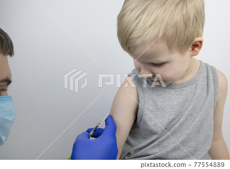A doctor injects a vaccine into the boy shoulder. The concept of vaccination of children and the prevention of infectious diseases. A doctor injects a vaccine into the boy shoulder. The concept of vaccination of children and the prevention of infectious diseases. 77554889