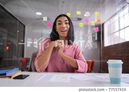 Happy mixed race businesswoman sitting at desk while having a video call smiling 77557410
