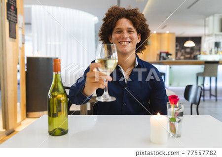 Mixed race man sitting at table in restaurant on dinner date smiling holding wine glass 77557782